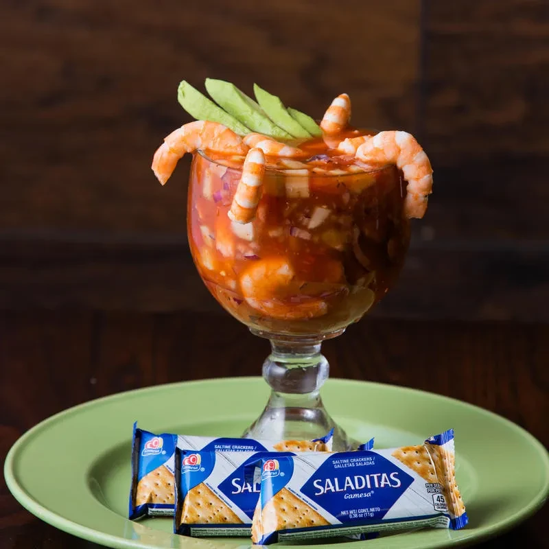 Shrimp cocktail in footed glass with avocado and saltine crackers.