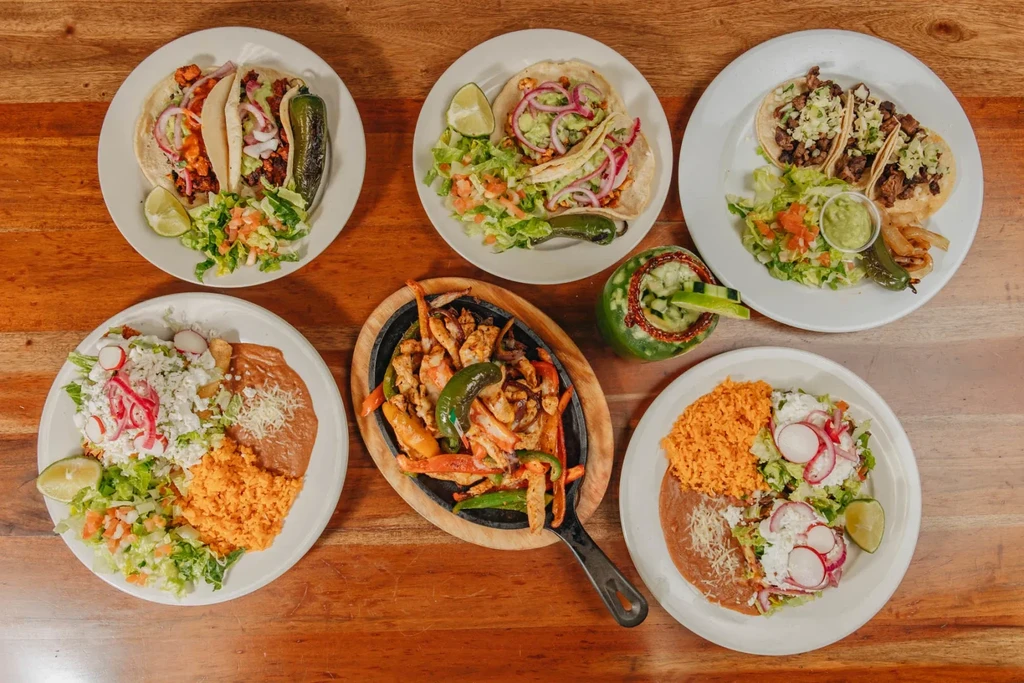 Overhead view of Mexican dishes, fajitas, and green drink on wood.