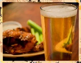 Pint of cold beer with condensation, blurred chicken wings and celery.