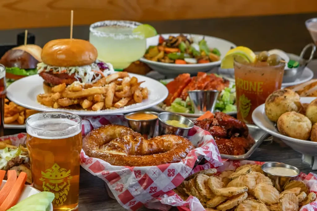 Wooden table covered with various pub food, beer, margaritas, and cocktails.