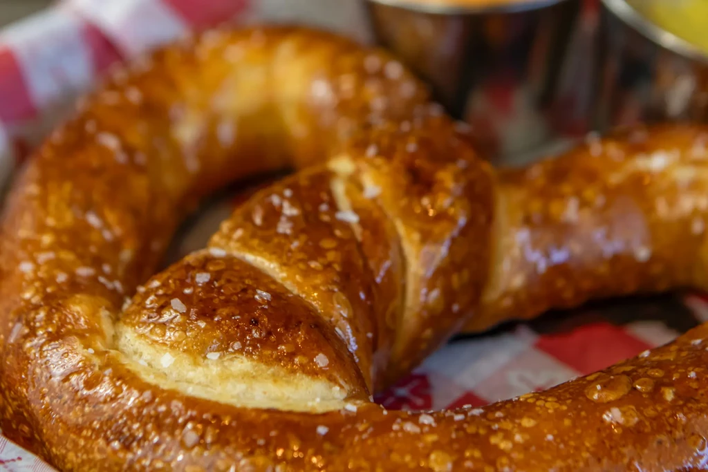 A close-up of a salted, golden-brown soft pretzel on checkered paper.