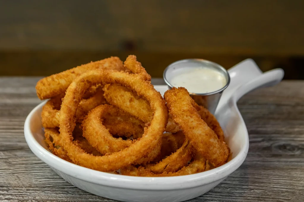 Golden-brown, crispy onion rings with dipping sauce in a white bowl.