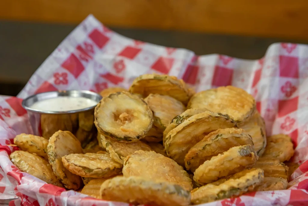 Fried pickles in a red checkered basket with creamy white sauce.