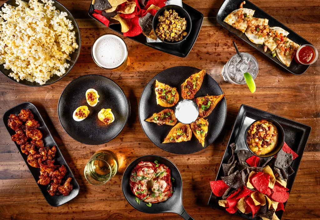 Flat lay of diverse appetizers, snacks, and drinks on a rustic table.