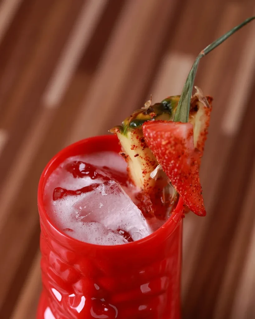 Close-up of a red tiki cocktail with spiced fruit and foam.