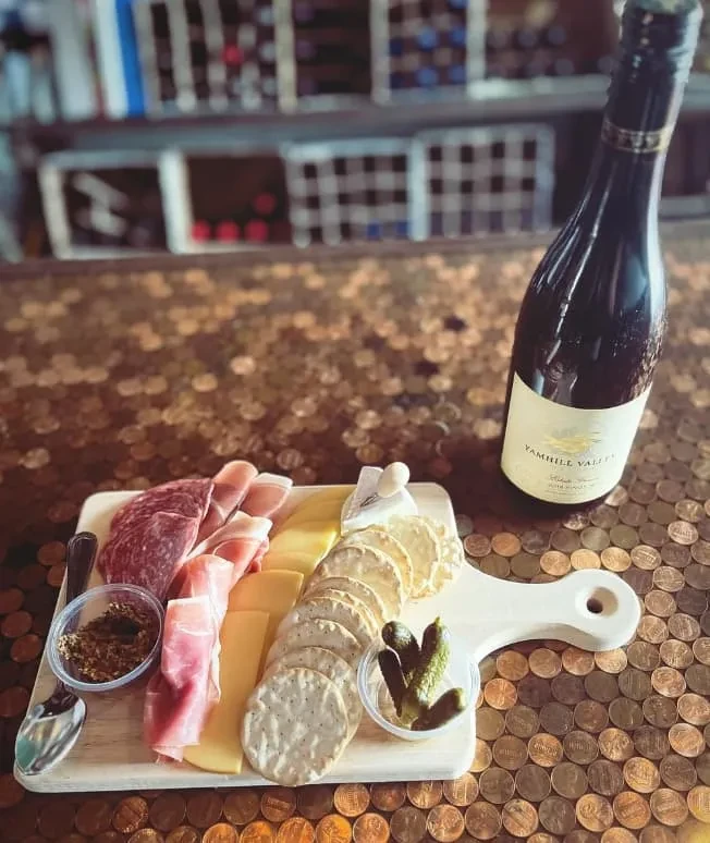 Charcuterie board, wine, and food on a copper penny mosaic surface.