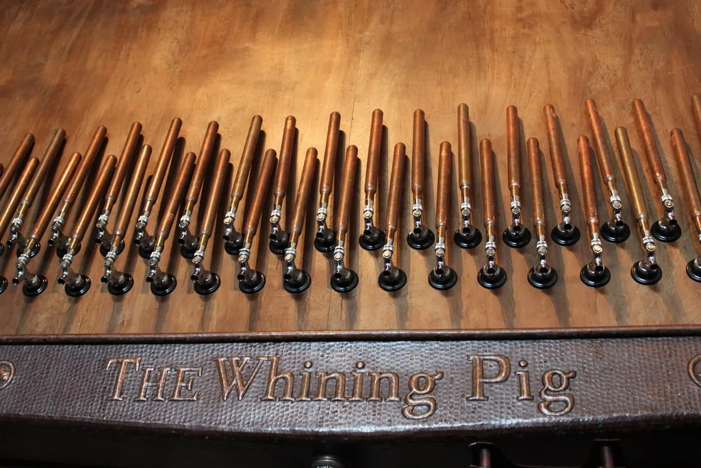 Copper beer taps above "THE Whining Pig" sign on a hammered panel.