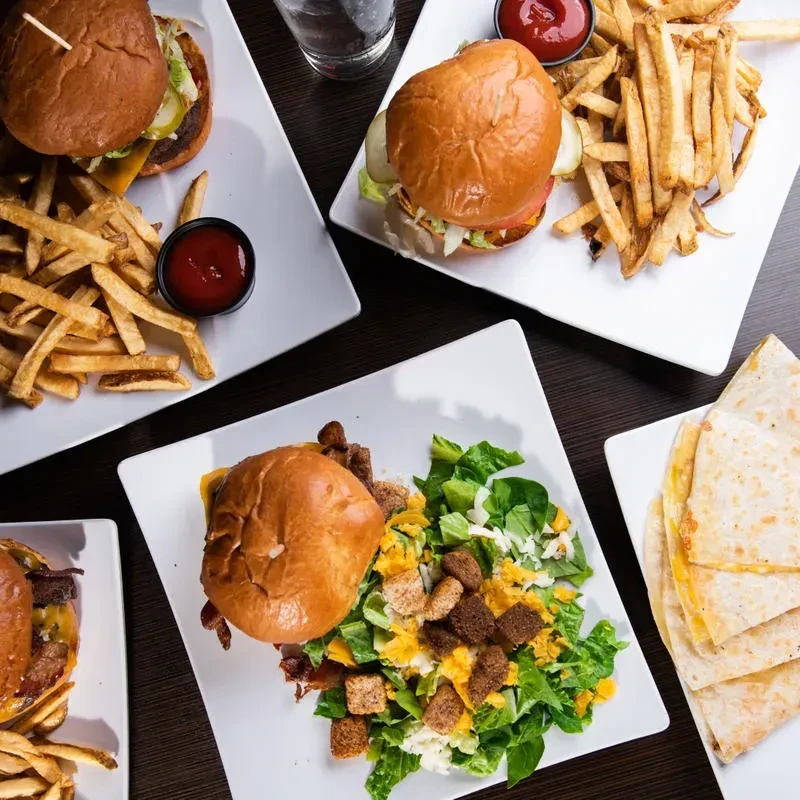 Overhead view of four plates with burgers, fries, salad, and quesadillas.