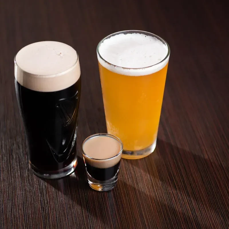 Three drinks: dark stout, layered shot, golden beer on wood.