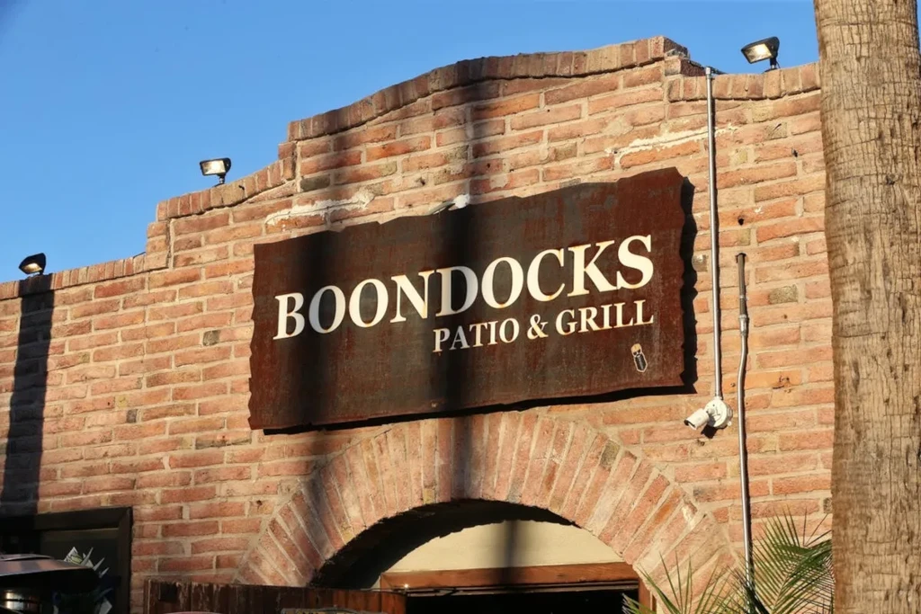 Rustic metal sign "BOONDOCKS PATIO & GRILL" on a brick facade.