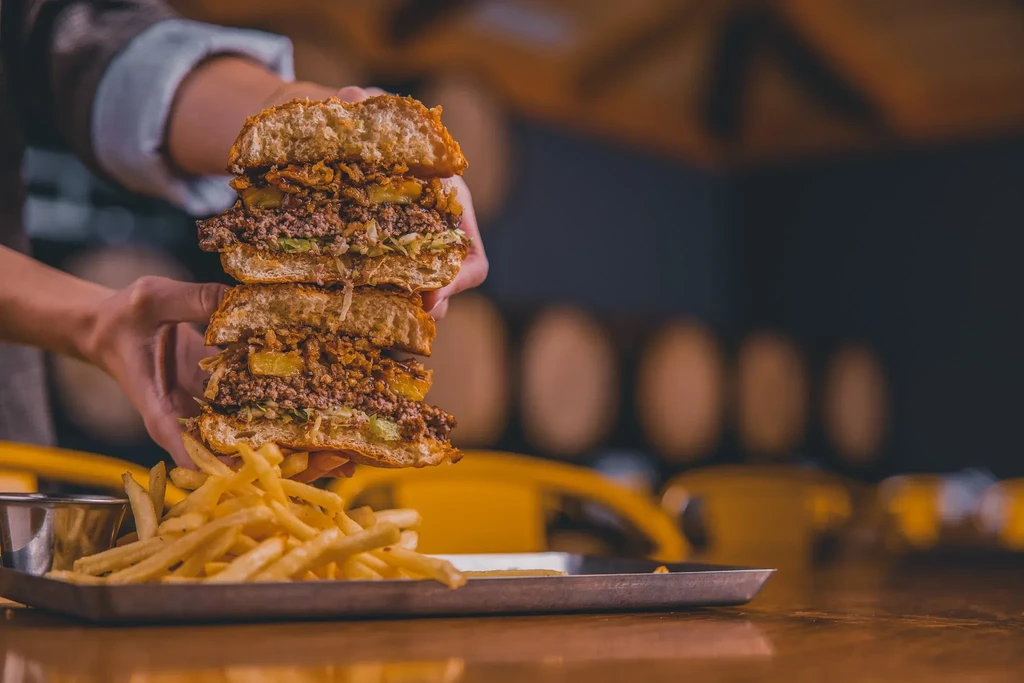 Close-up of hands holding a sliced, multi-layered burger with fries.