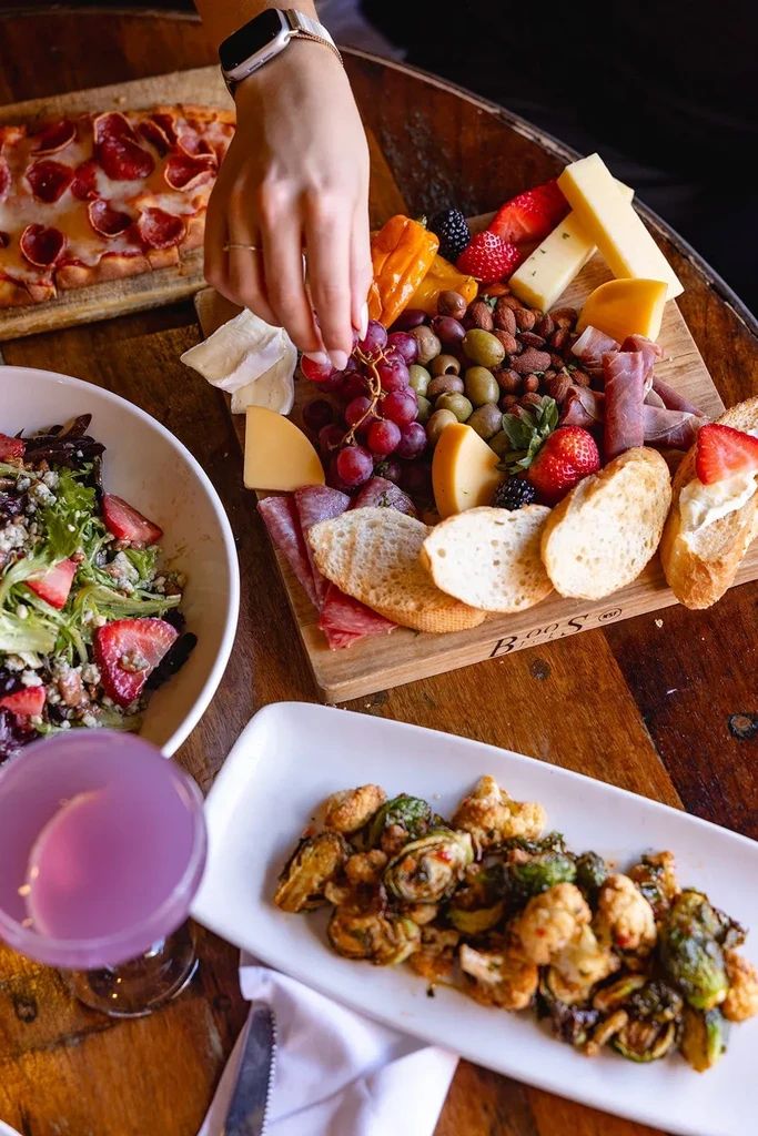 Rustic table with a diverse meal spread and a hand reaching for food.