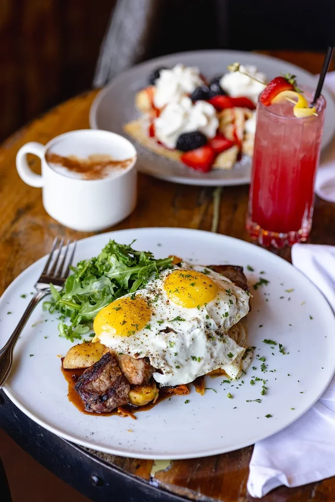 Breakfast plate with seared meat, fried eggs, potatoes, and arugula.