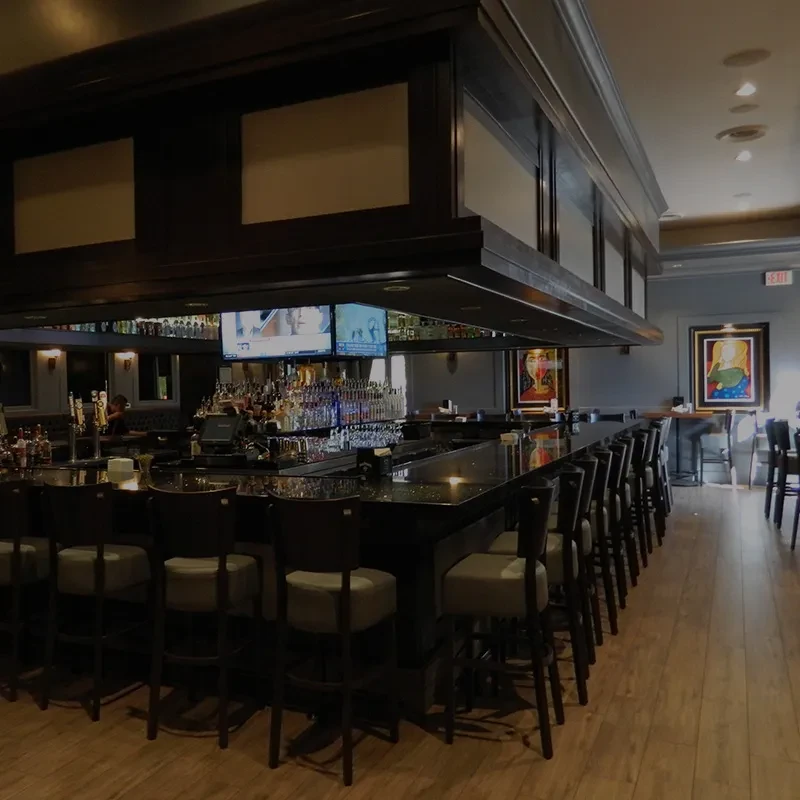 Elegant bar with a long dark counter, illuminated bottles, and TVs.