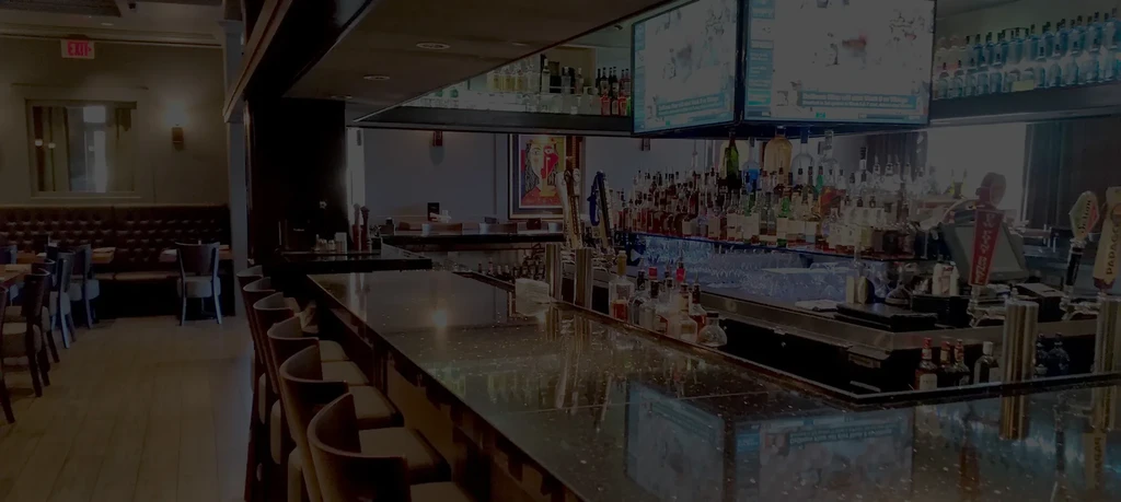 Dark, modern restaurant bar interior with TVs, stools, and booths.
