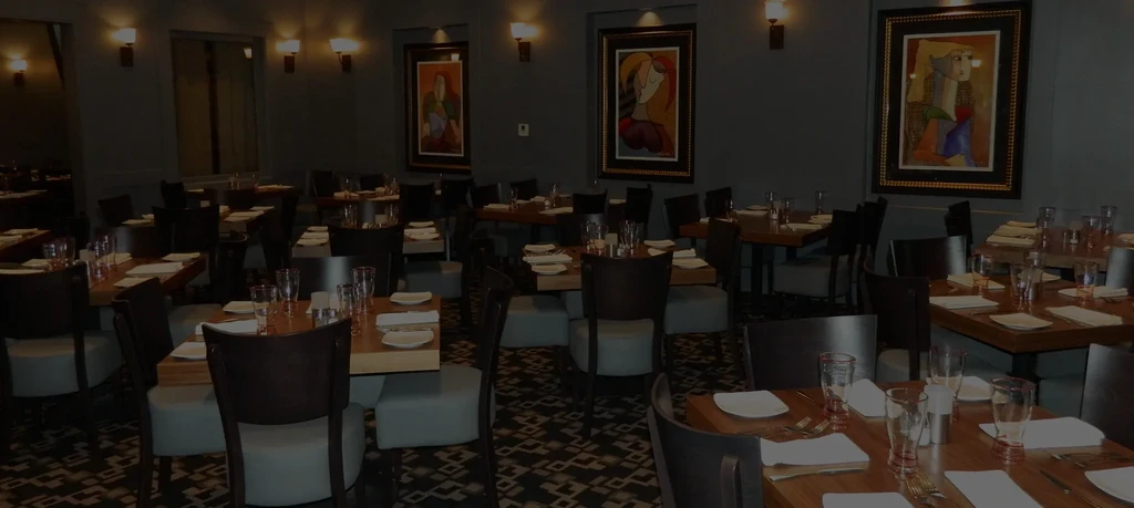 Dimly lit empty restaurant dining room with set tables, abstract art.