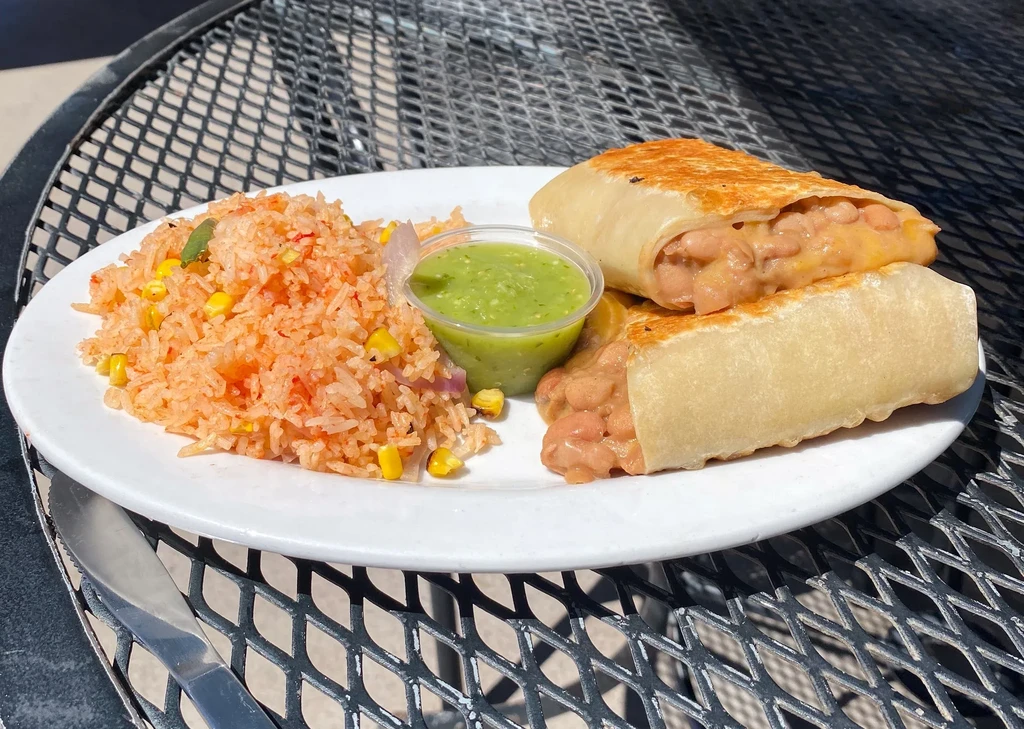 Deep-fried burritos, rice, and salsa verde served on an outdoor table.