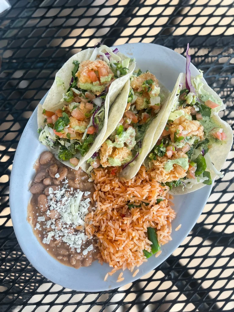 Overhead view of three tacos, refried beans, and Mexican rice.