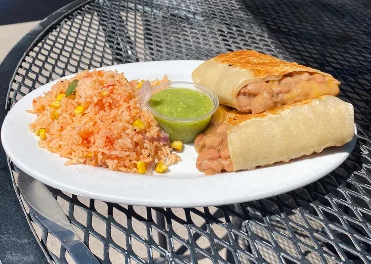 Sunny outdoor plate of Mexican rice, cut burritos, and green salsa.