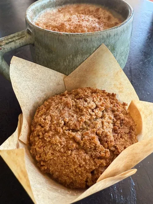 Overhead close-up of a crumb-topped muffin and a foamy latte.