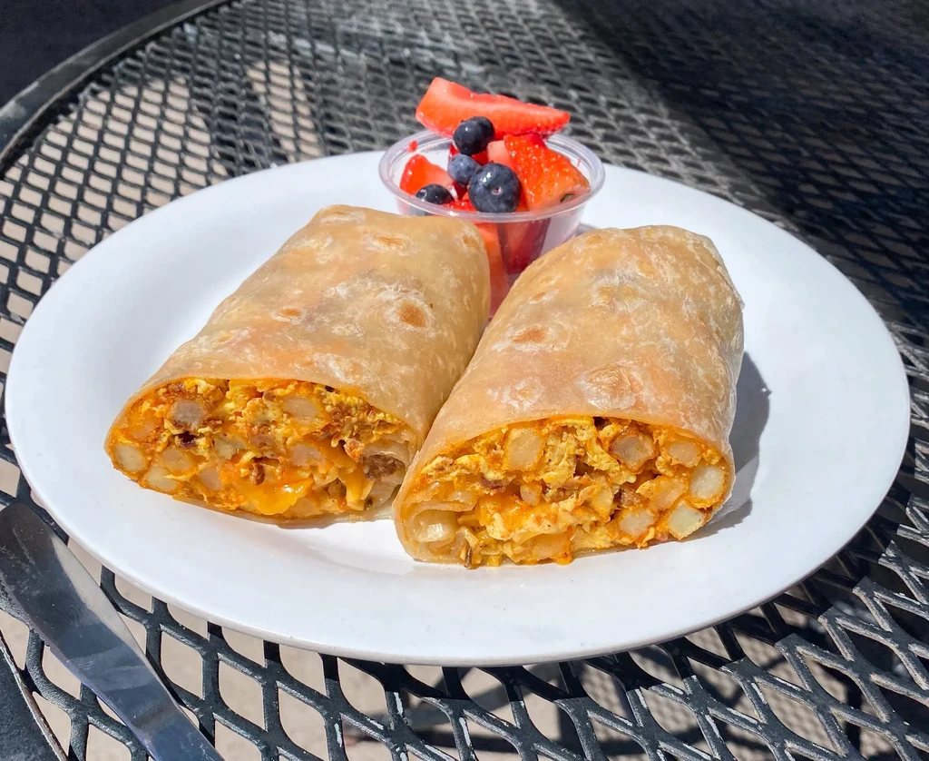 Halved crispy breakfast burritos showing eggs, cheese, meat, and fruit salad.