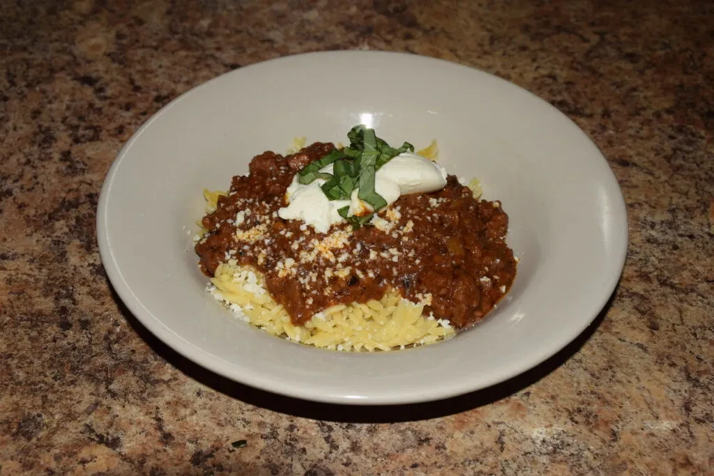 Orzo pasta with meat sauce, cheese, creamy topping, spice, and basil.