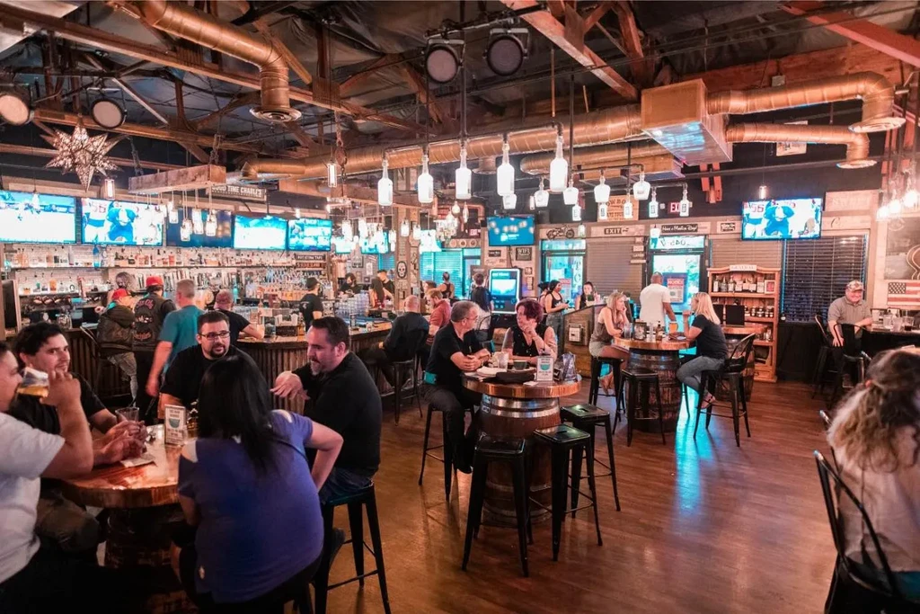 Bustling rustic-industrial bar interior, many patrons, unique bottle lights.