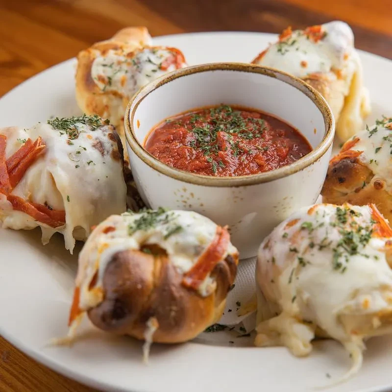 Plate of cheesy baked knots with pepperoni, herbs, and marinara dipping sauce.