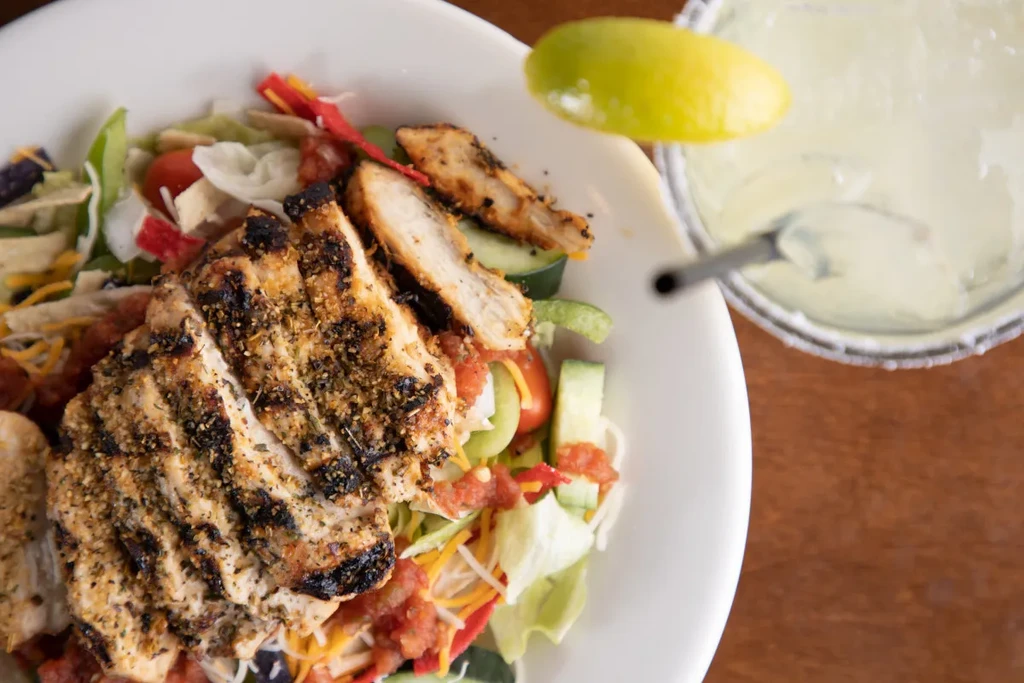 Close-up: Grilled chicken salad with a margarita on a wooden surface.