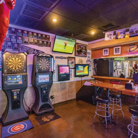 Empty sports bar with dartboards, TVs, a bar, and tables.