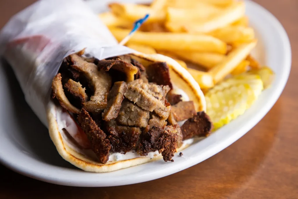 Gyro with grilled meat, french fries, and pickles on a plate.