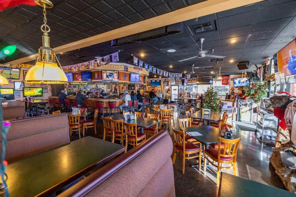 Lively sports bar interior with people, TVs, festive trees, and a bear.
