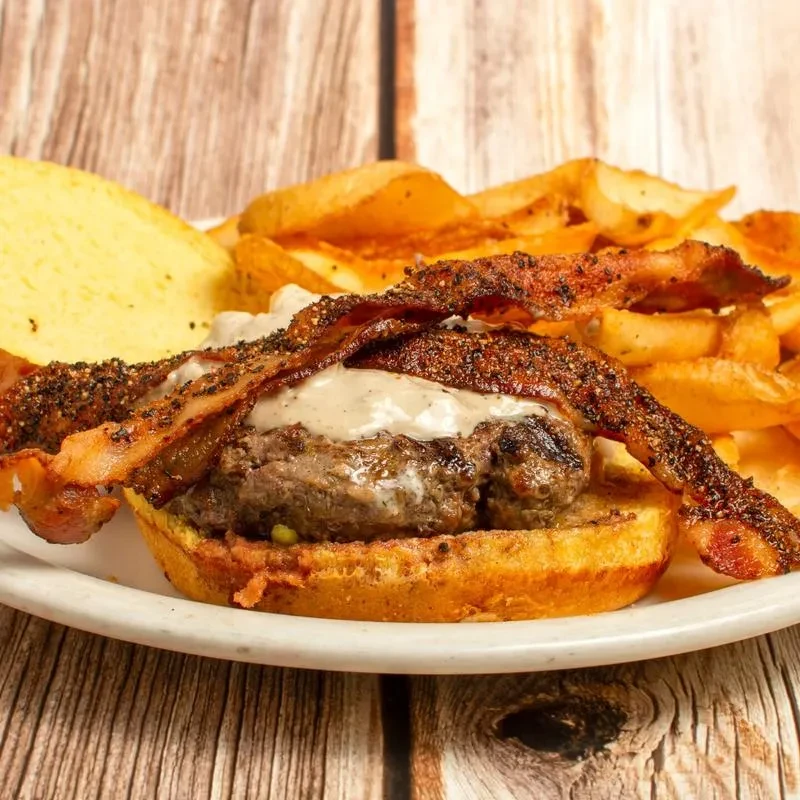 Gourmet burger with bacon, creamy sauce, and wedge fries.