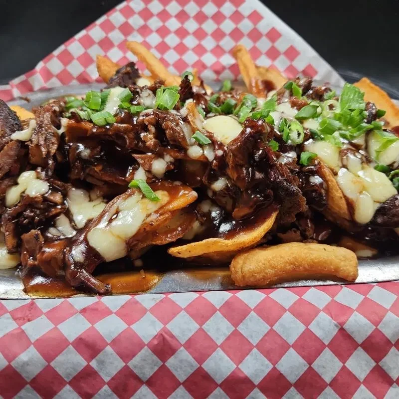 Close-up of loaded fries with gravy, cheese, shredded meat, green onions.