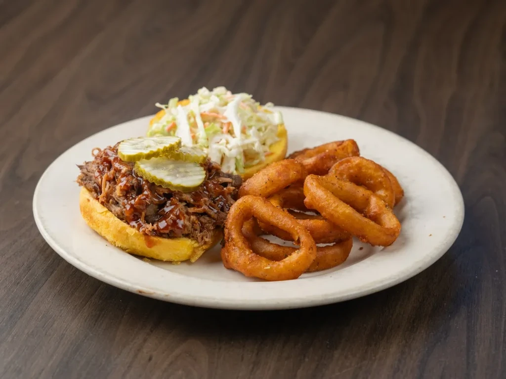 Pulled pork sandwich, coleslaw, and onion rings on a white plate.