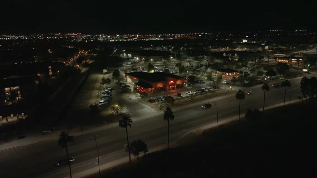 Aerial night shot of a brightly lit restaurant with patio and cars.