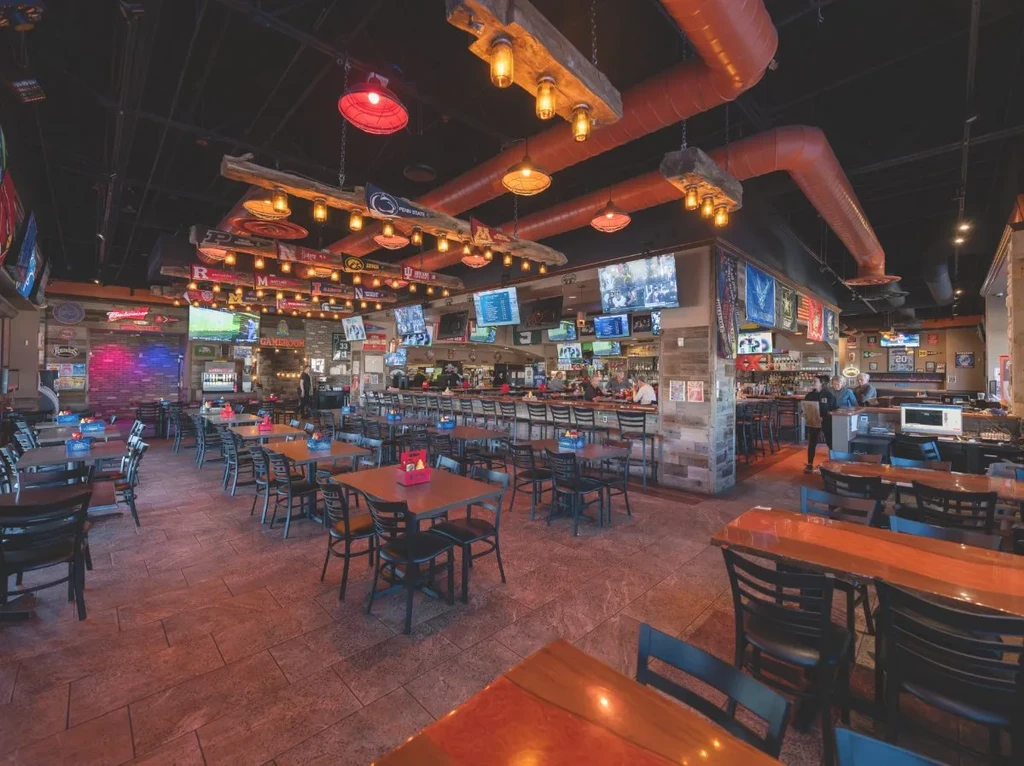 Well-lit sports bar interior with TVs, college pennants, and a long bar.