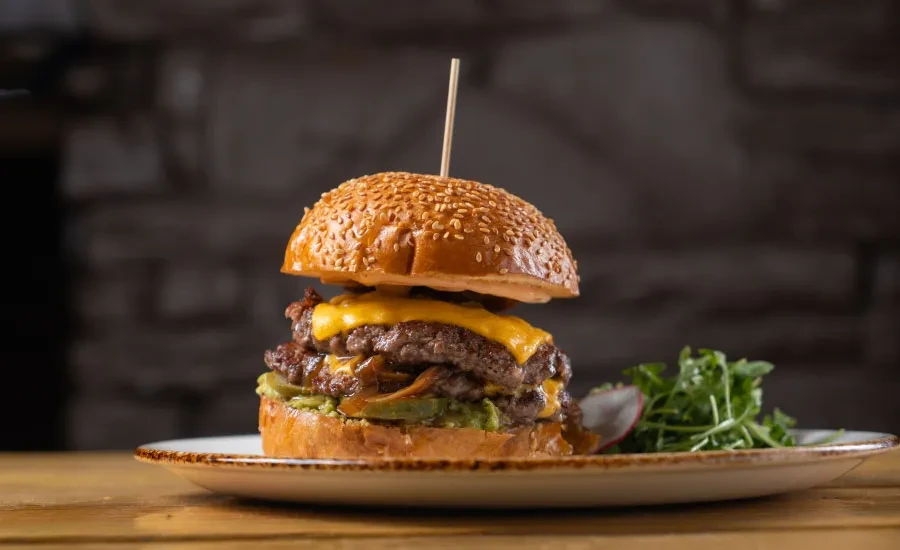 Double cheeseburger held by skewer, with arugula and radish.