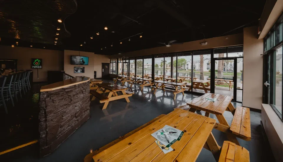 Empty modern restaurant interior with bar, picnic tables, and lake view.