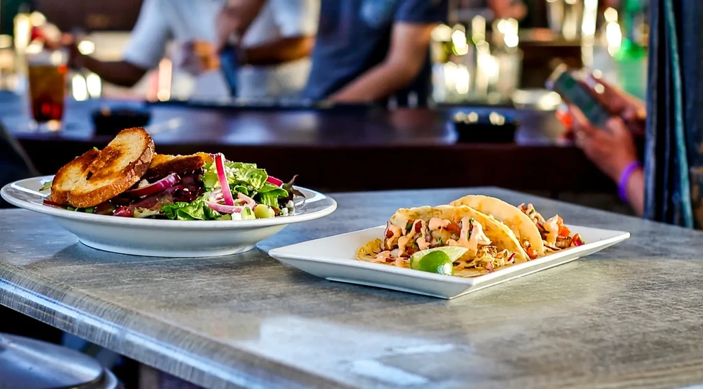 Two dishes: a fresh salad and two tacos on a grey counter.
