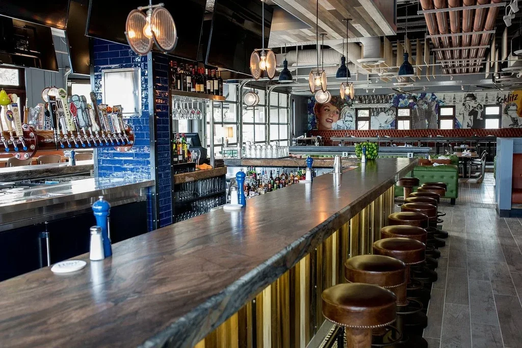 Modern restaurant bar with natural-edge wood counter, stools, and artistic murals.