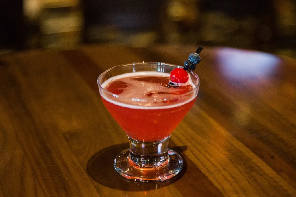 Vibrant red cocktail with cherry and blueberries on a wooden table.