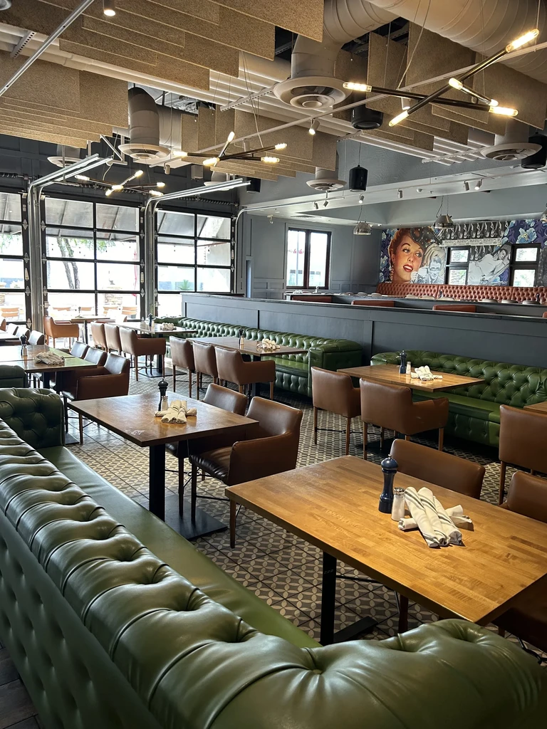 Restaurant interior: green booths, geometric floor, industrial lighting, vintage mural.