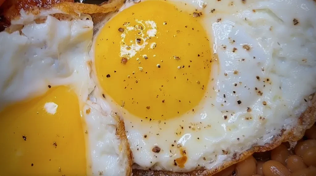 Two sunny-side-up eggs with pepper, crispy edges, and baked beans.