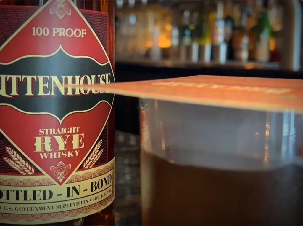 Close-up of Rittenhouse Rye bottle and whisky glass in a bar.
