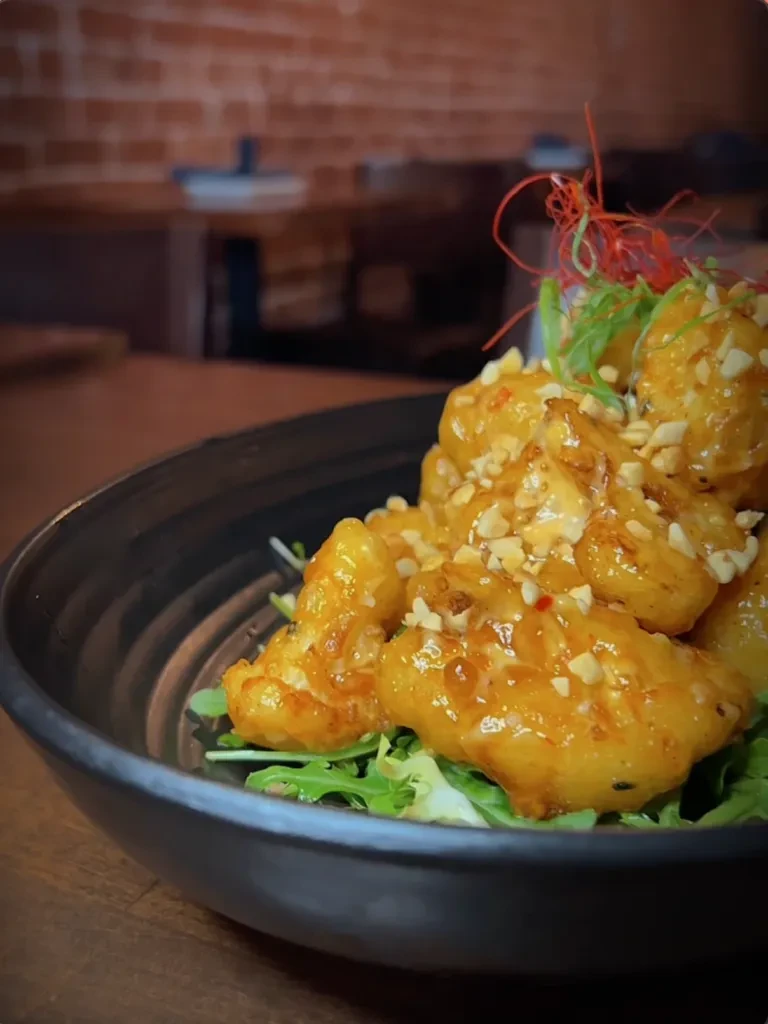 Close-up of battered food with orange sauce, peanuts, and greens.