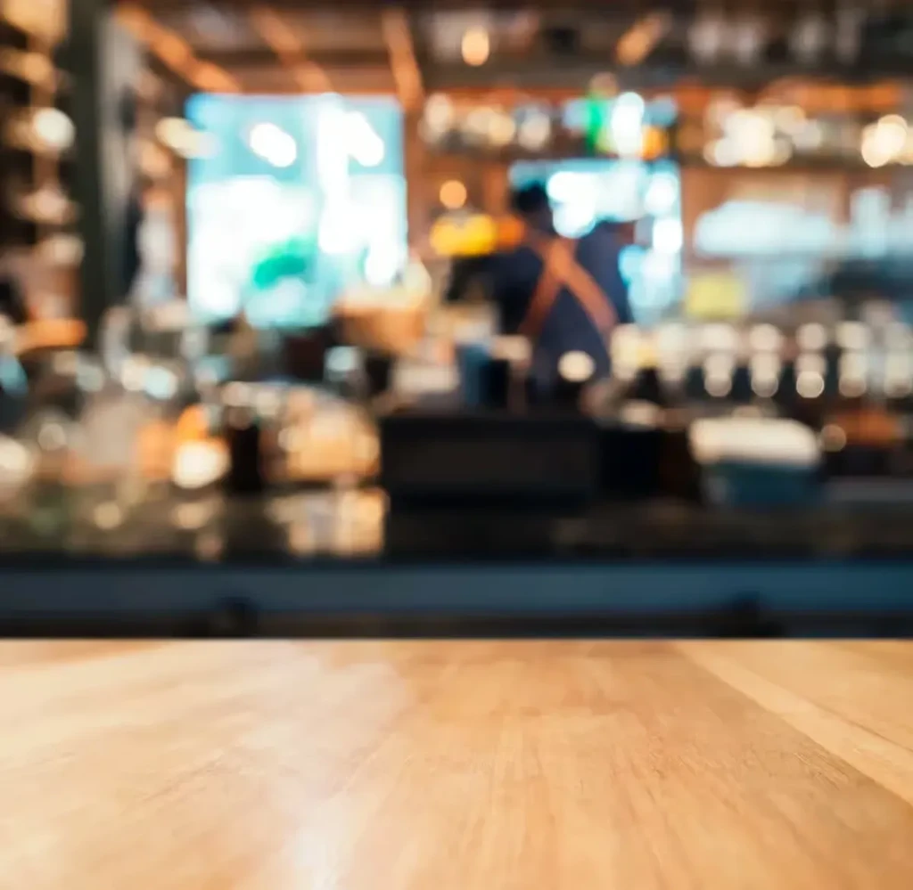 Wooden bar top in sharp focus, blurred cafe interior and person.