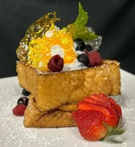Stacked golden French toast, berries, cream, sugar art, and fanned strawberry.