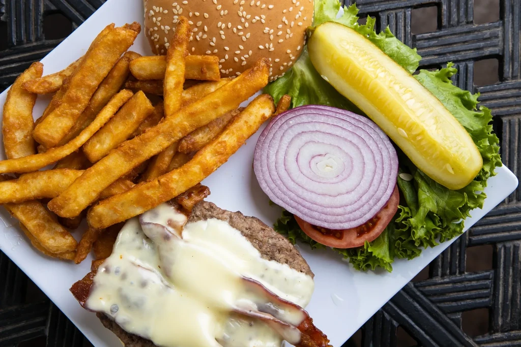 Overhead view: Deconstructed burger with cheese, bacon, fries, garnishes.