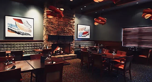 Elegant restaurant interior with a warm stone fireplace, booths, and abstract art.
